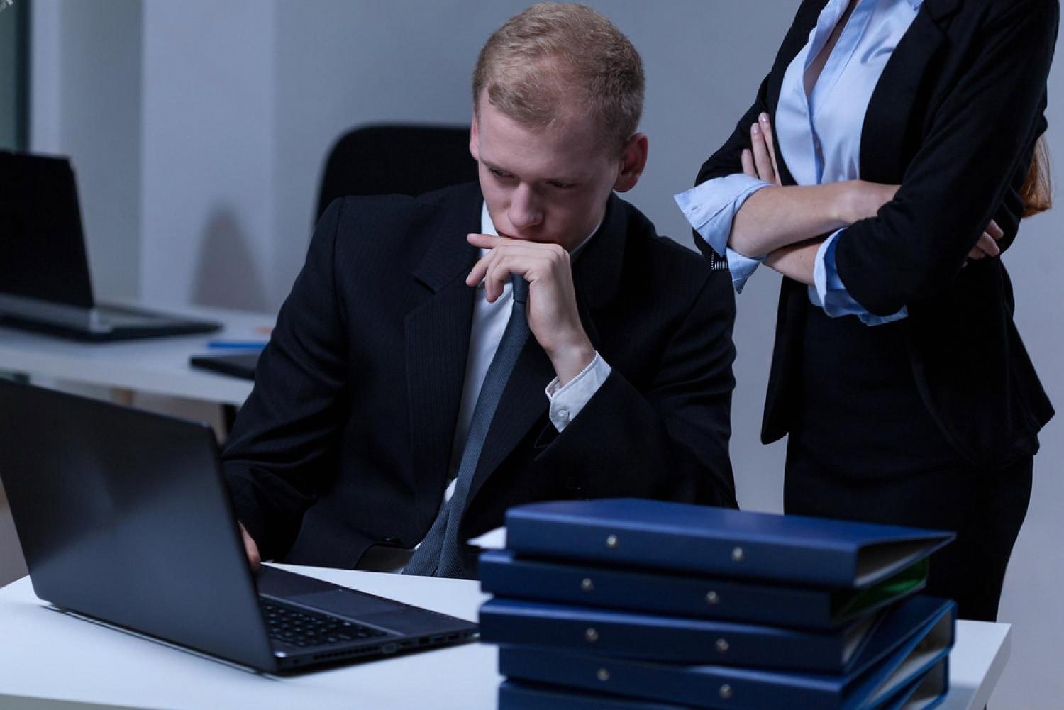 Businessman reviewing files on a laptop while a colleague waits, representing background checks on UAE partners